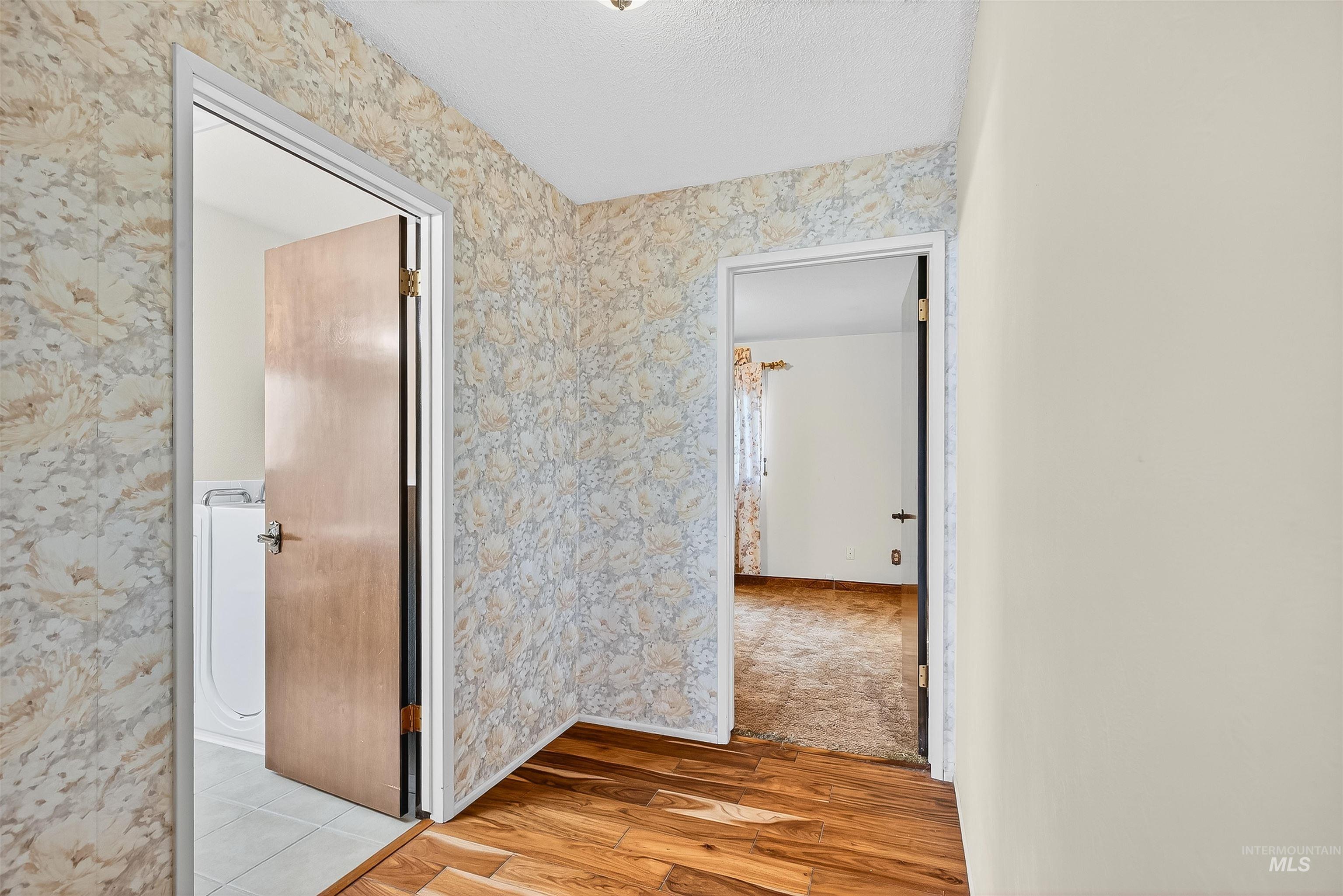 Hall with light wood-style floors, wallpapered walls, and a textured ceiling