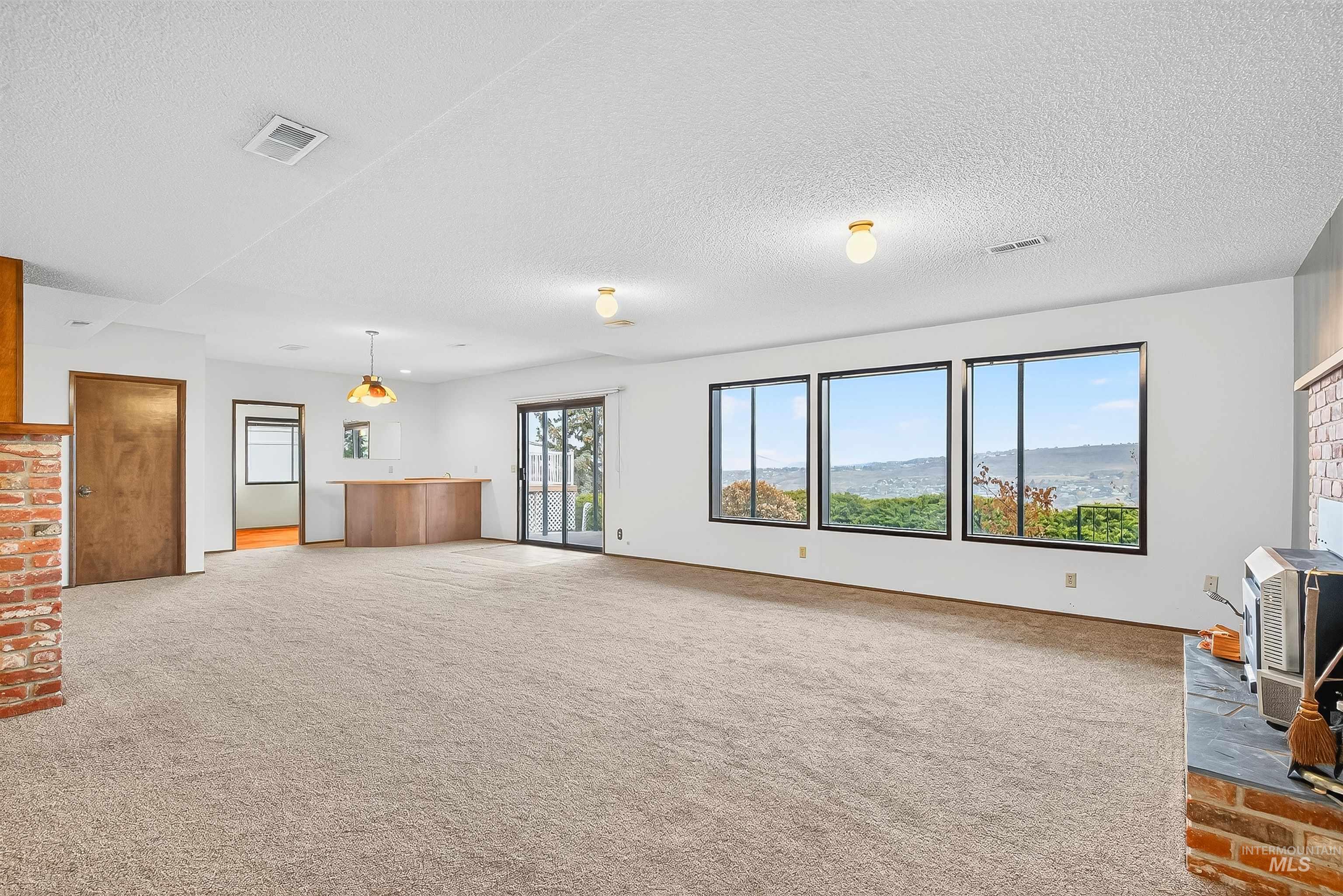 Unfurnished living room featuring a wood stove, light colored carpet, and a textured ceiling