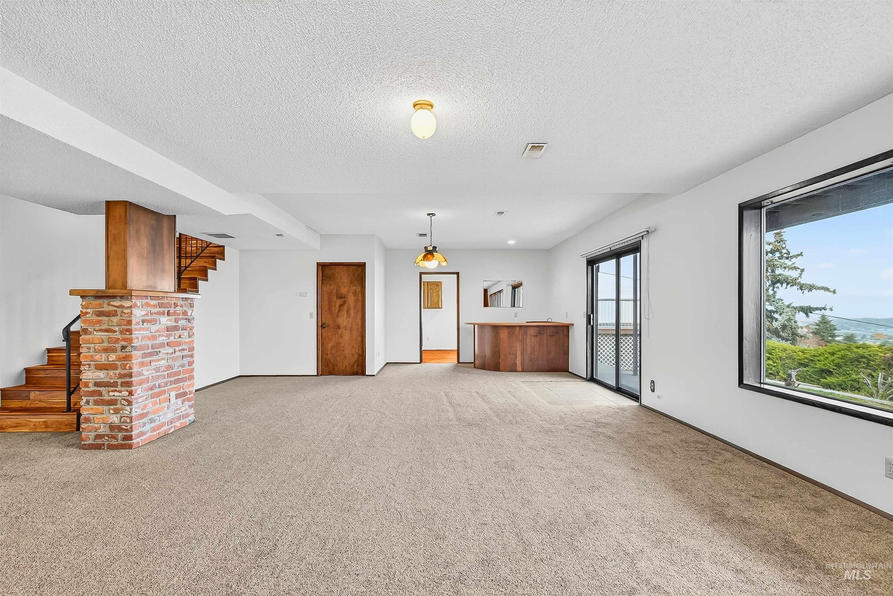 Unfurnished living room with light carpet, stairway, and a textured ceiling