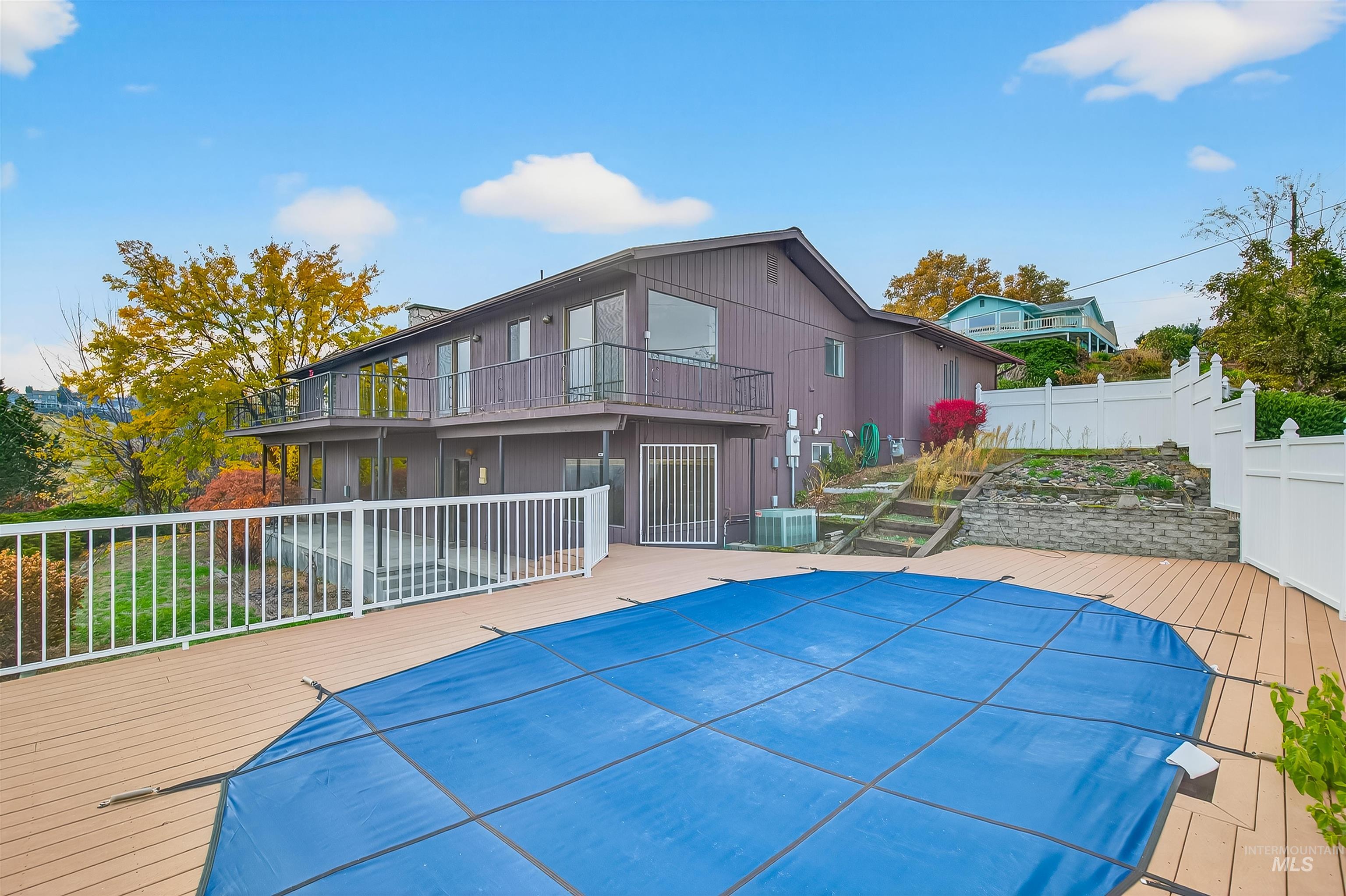 Back of property with a wooden deck, a patio area, and a covered pool