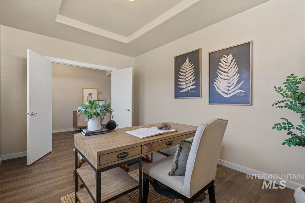 Home office featuring a tray ceiling and dark wood-type flooring