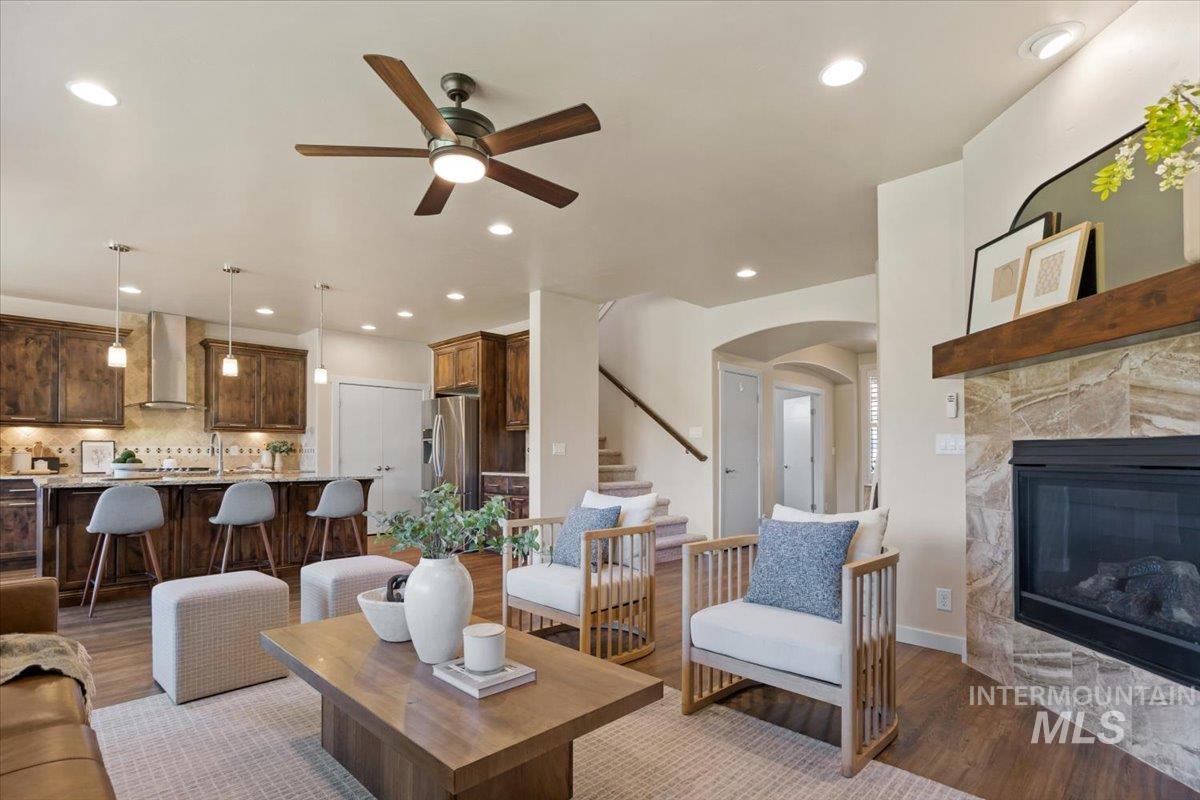Living room featuring light wood-style flooring, stairs, a ceiling fan, arched walkways, and a fireplace
