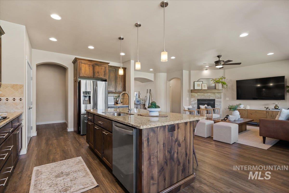 Kitchen featuring arched walkways, hanging light fixtures, appliances with stainless steel finishes, dark wood-style floors, and open floor plan