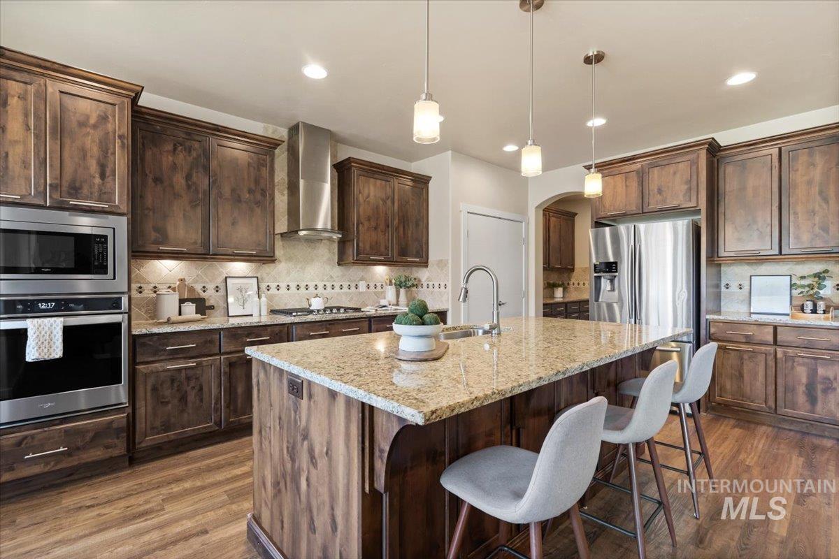 Kitchen with stainless steel appliances, light stone countertops, tasteful backsplash, arched walkways, and pendant lighting