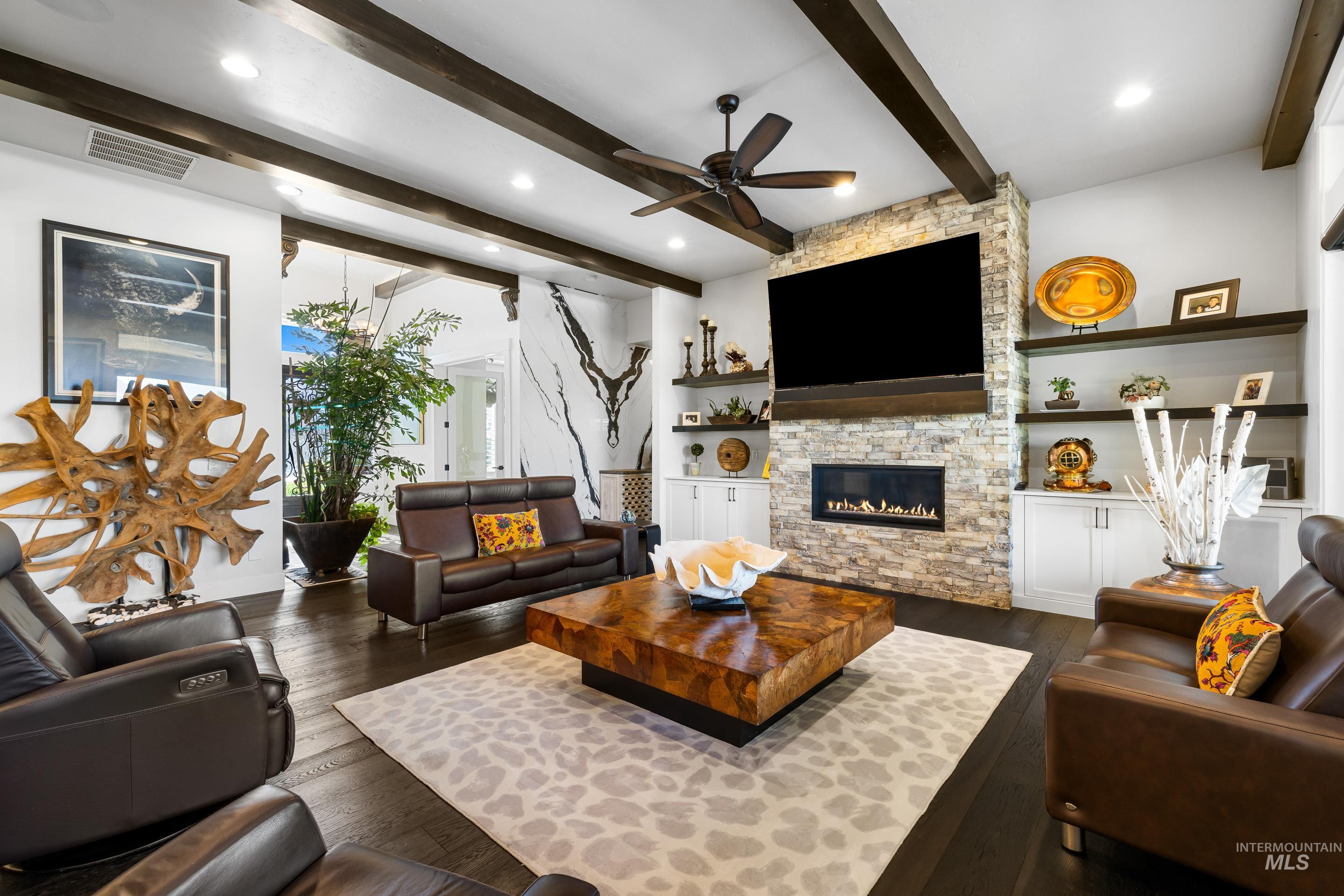 Living area with dark wood-style floors, a stone fireplace, beam ceiling, ceiling fan, and recessed lighting