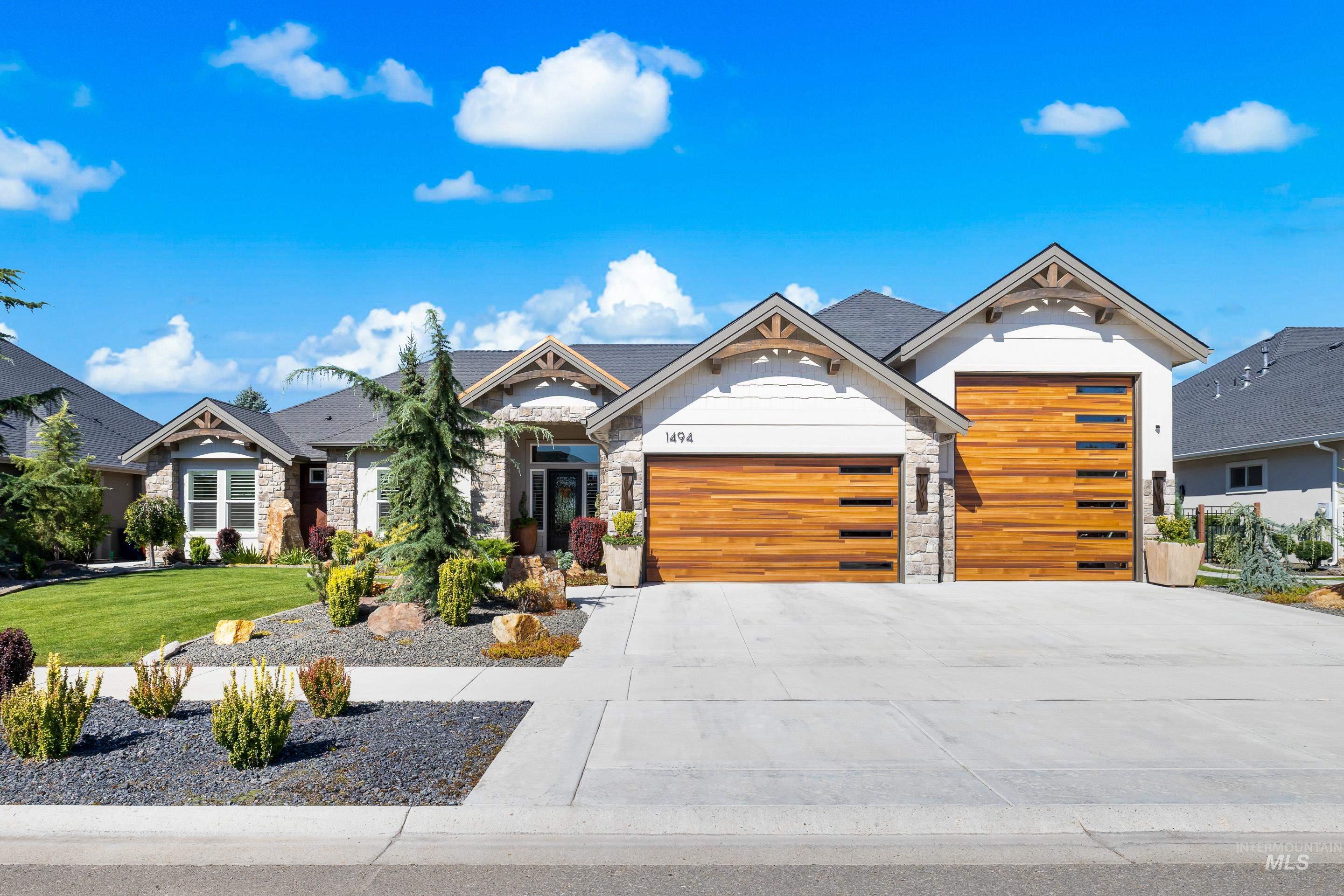 View of front of home with stone siding, driveway, a front lawn, and a garage