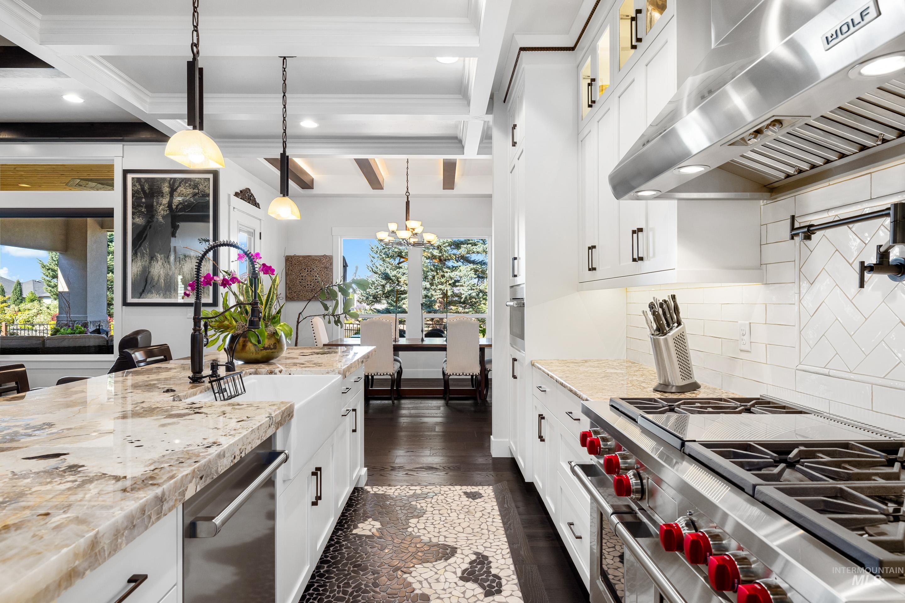 Kitchen featuring beam ceiling, ventilation hood, appliances with stainless steel finishes, decorative light fixtures, and white cabinetry