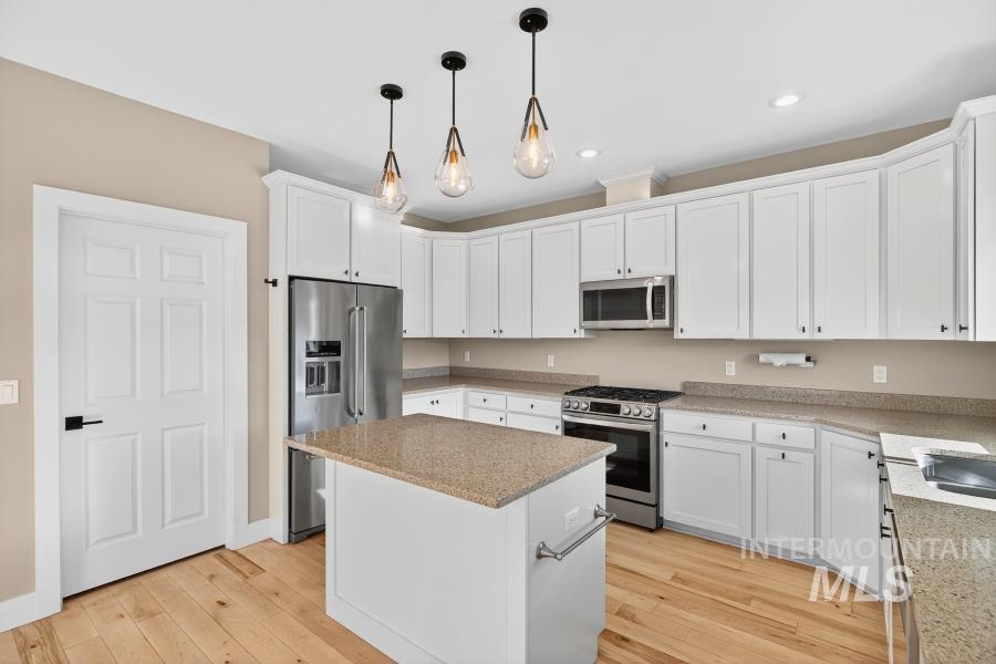 Kitchen featuring stainless steel appliances, white cabinets, decorative light fixtures, light wood-type flooring, and a center island