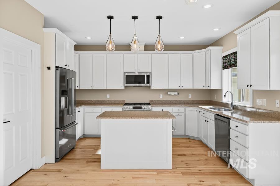 Kitchen featuring stainless steel appliances, white cabinets, decorative light fixtures, a kitchen island, and recessed lighting