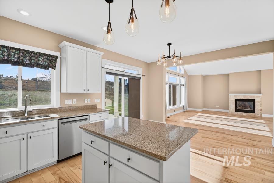 Kitchen with light wood finished floors, pendant lighting, white cabinetry, light stone countertops, and dishwasher