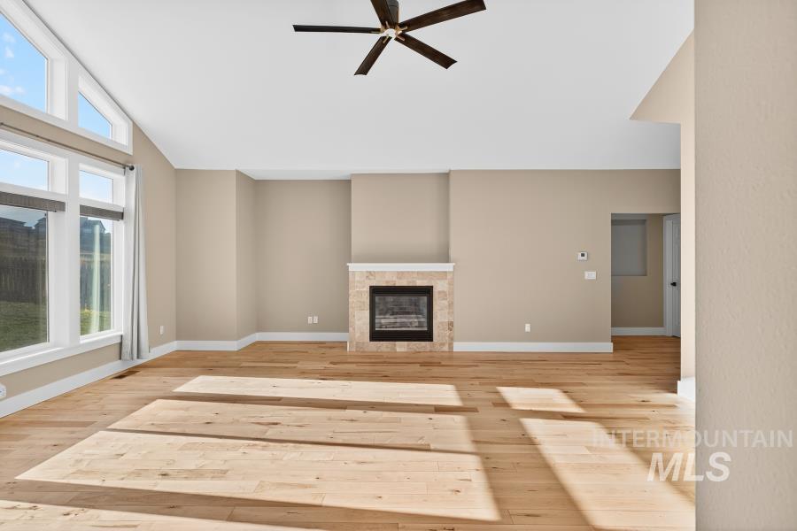Unfurnished living room with a tiled fireplace, light wood-type flooring, a ceiling fan, and vaulted ceiling