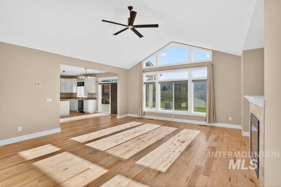 Unfurnished living room with a fireplace, high vaulted ceiling, light wood finished floors, a ceiling fan, and a chandelier