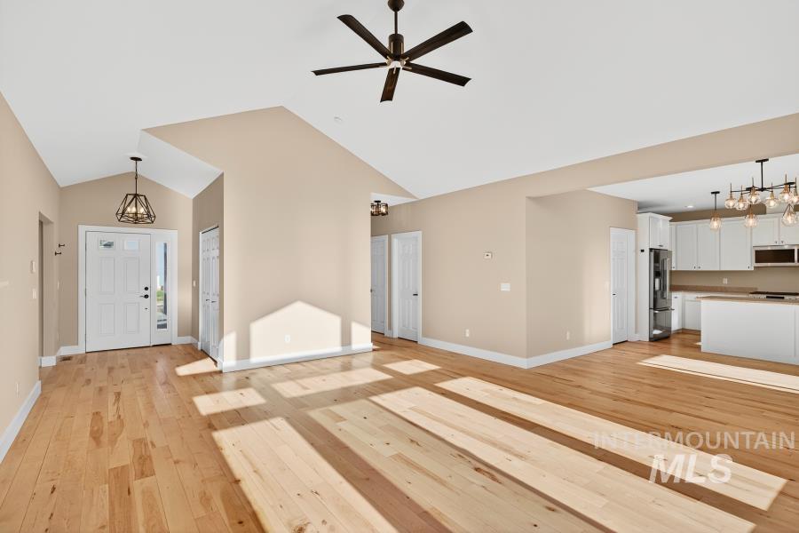 Unfurnished living room featuring a chandelier, light wood-type flooring, high vaulted ceiling, and ceiling fan