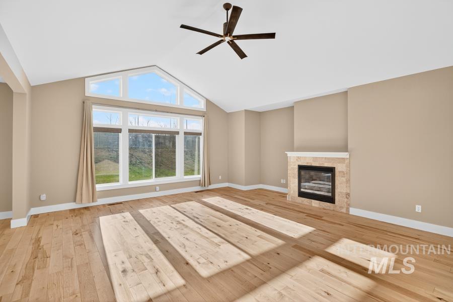 Unfurnished living room with a glass covered fireplace, ceiling fan, light wood-style flooring, and high vaulted ceiling