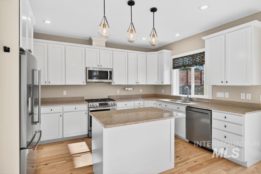 Kitchen featuring appliances with stainless steel finishes, white cabinetry, decorative light fixtures, light wood-style floors, and light stone countertops