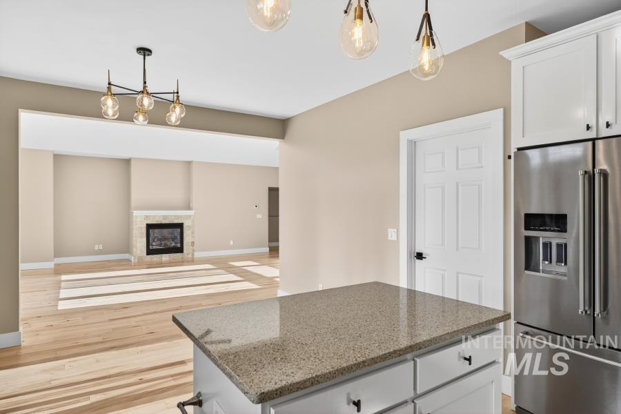 Kitchen featuring hanging light fixtures, high quality fridge, white cabinets, light wood finished floors, and light stone counters