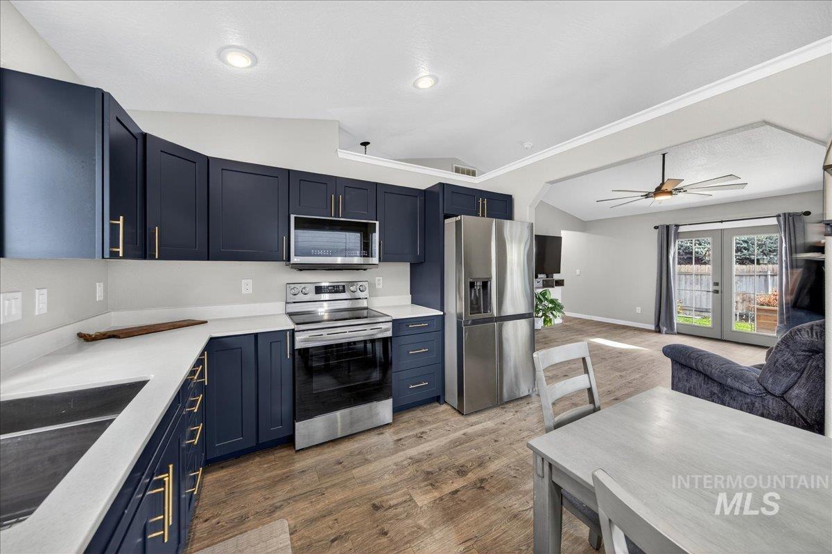 Kitchen featuring vaulted ceiling, appliances with stainless steel finishes, light stone countertops, blue cabinetry, and dark wood-style floors