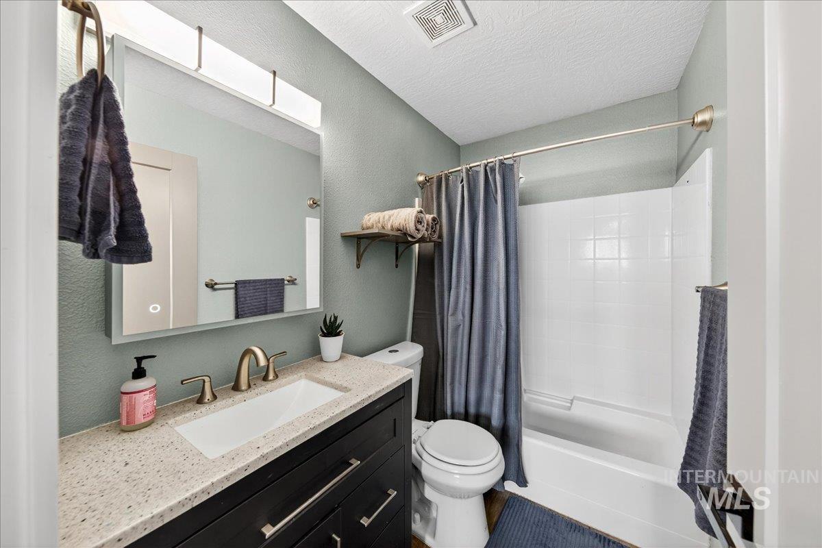 Bathroom with shower / bath combo, vanity, a textured ceiling, and a textured wall