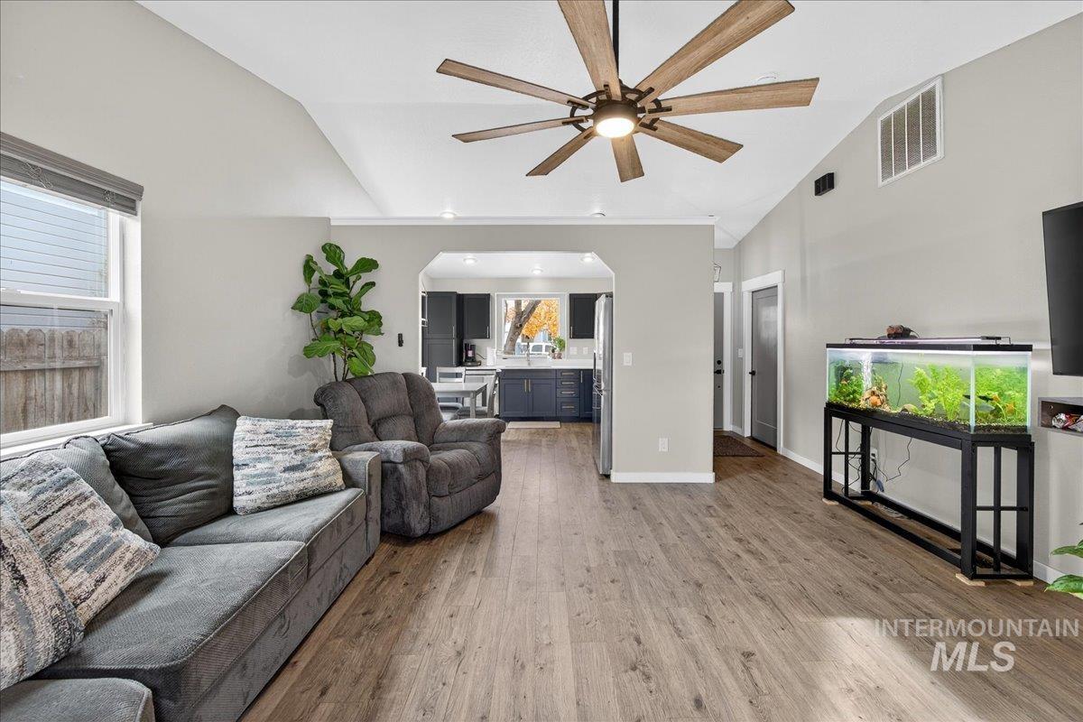 Living room featuring light wood-type flooring, arched walkways, a ceiling fan, and high vaulted ceiling