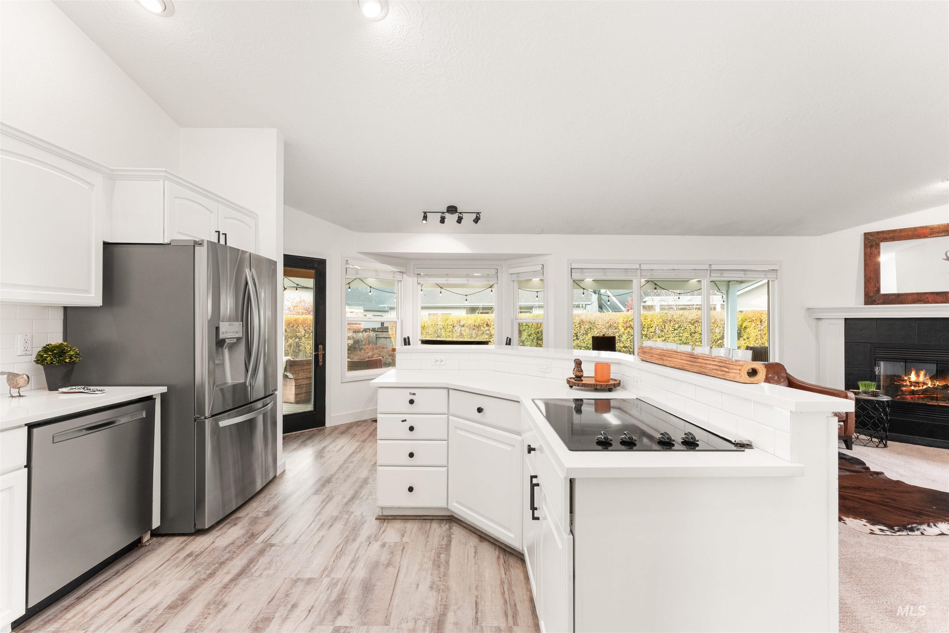 Kitchen with white cabinetry, a glass covered fireplace, appliances with stainless steel finishes, light countertops, and lofted ceiling