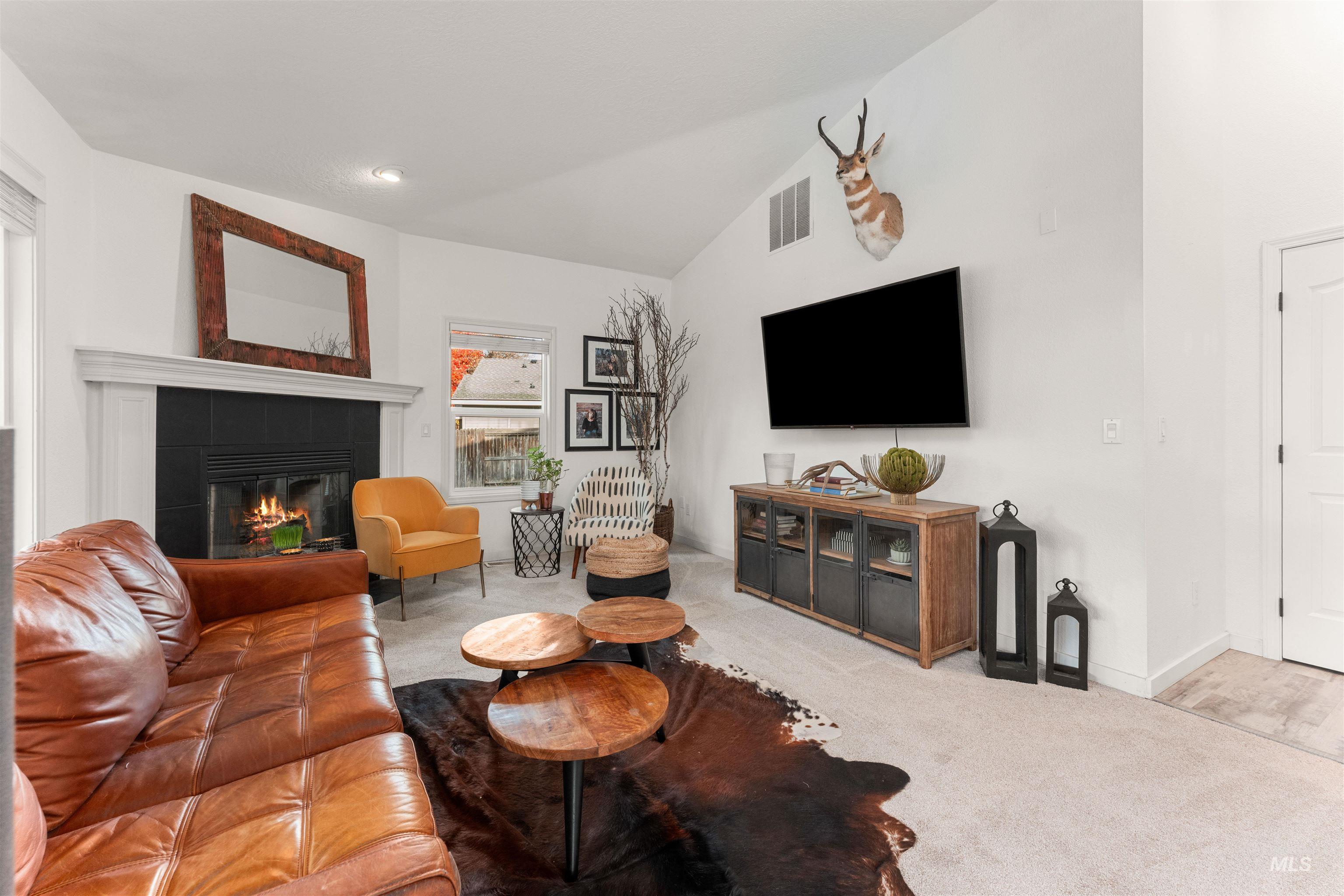 Living room with vaulted ceiling, a tiled fireplace, and light carpet