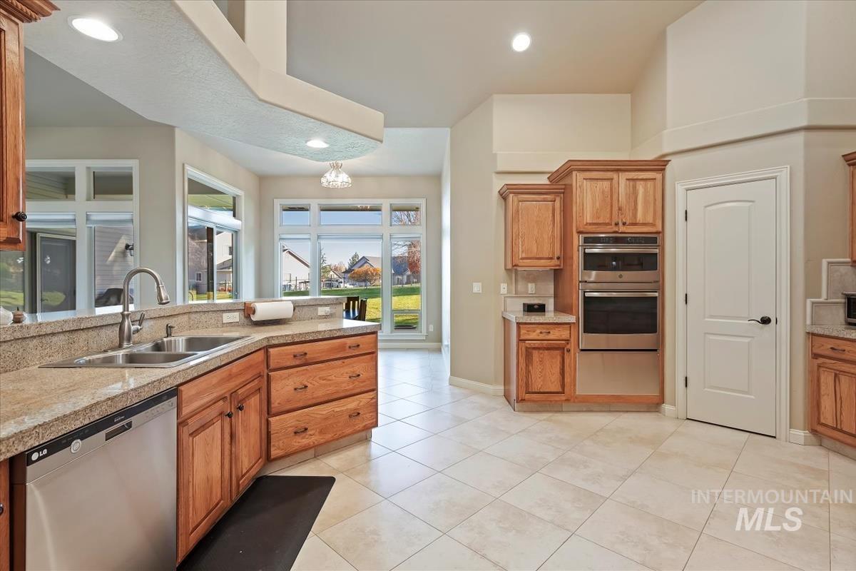 Kitchen with appliances with stainless steel finishes, brown cabinetry, light tile patterned flooring, recessed lighting, and a chandelier