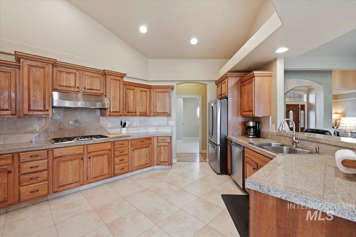 Kitchen featuring arched walkways, light countertops, decorative backsplash, brown cabinetry, and recessed lighting