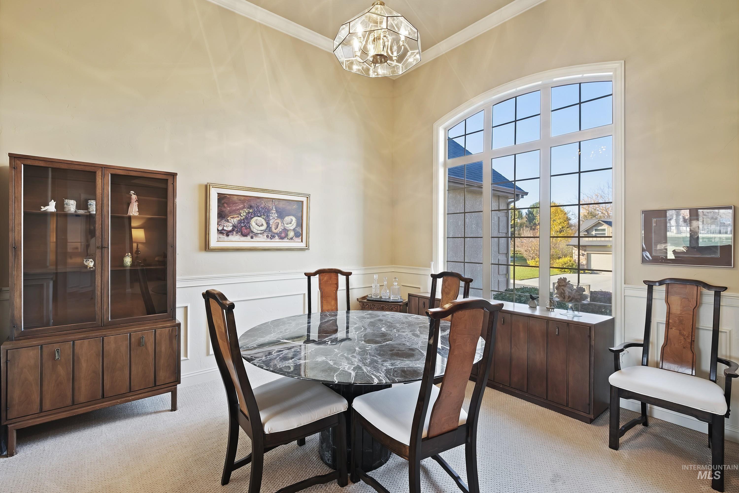 Dining space featuring light colored carpet, ornamental molding, a wainscoted wall, a chandelier, and a decorative wall