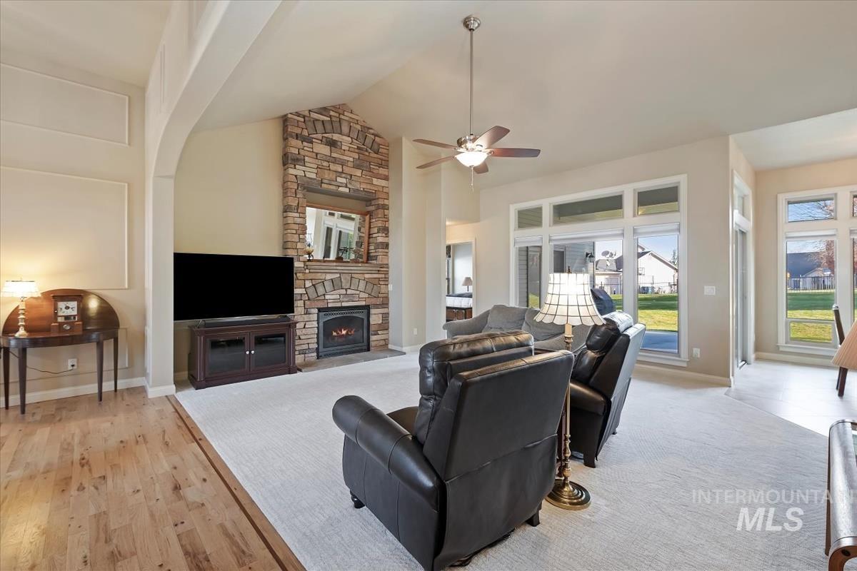 Living room featuring a fireplace, high vaulted ceiling, ceiling fan, and light wood-type flooring