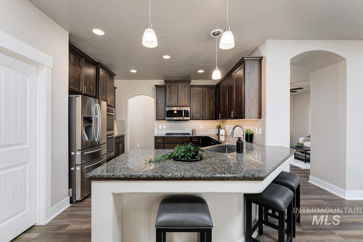 Kitchen featuring arched walkways, dark brown cabinetry, backsplash, appliances with stainless steel finishes, and dark wood finished floors