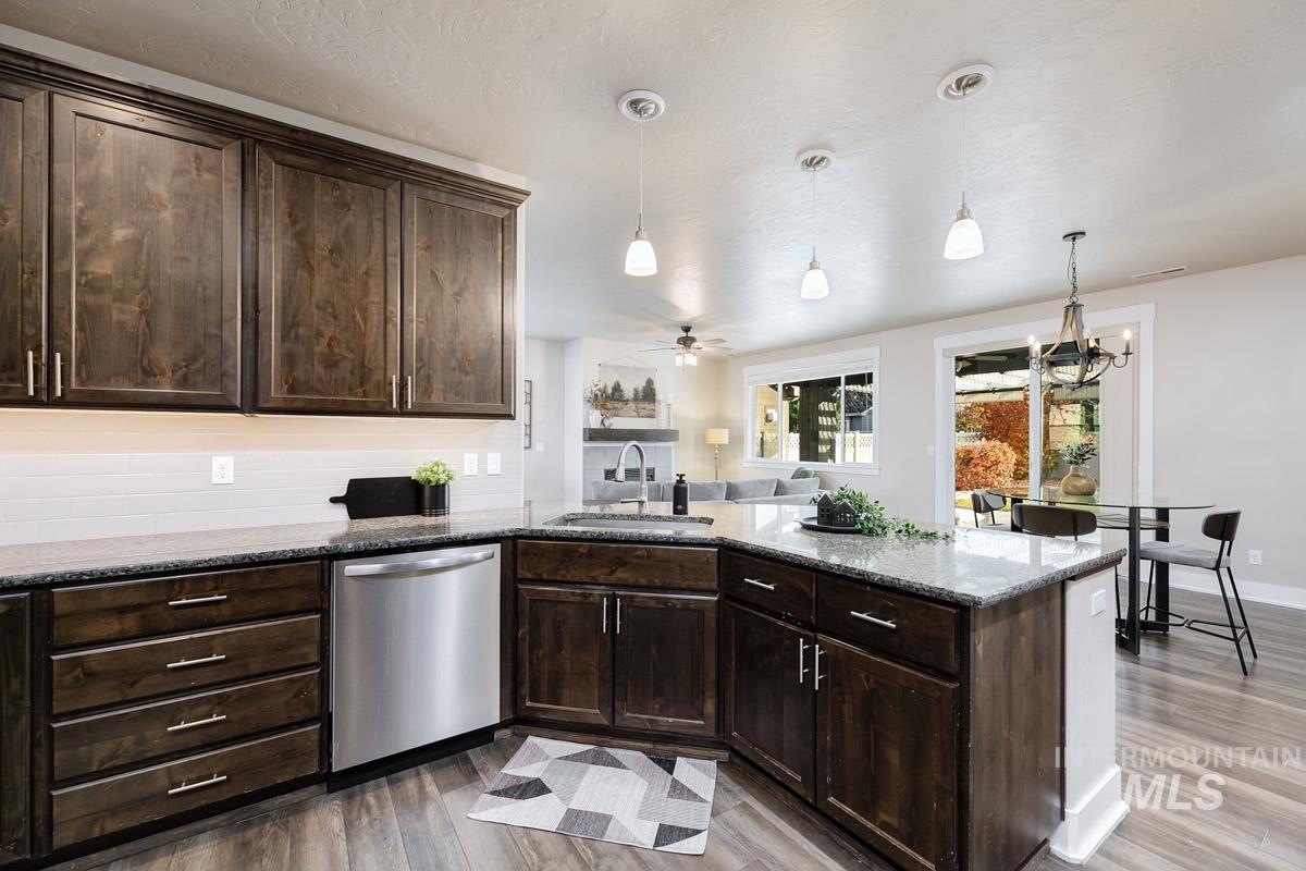 Kitchen with dark brown cabinetry, dark stone counters, hanging light fixtures, and dishwasher