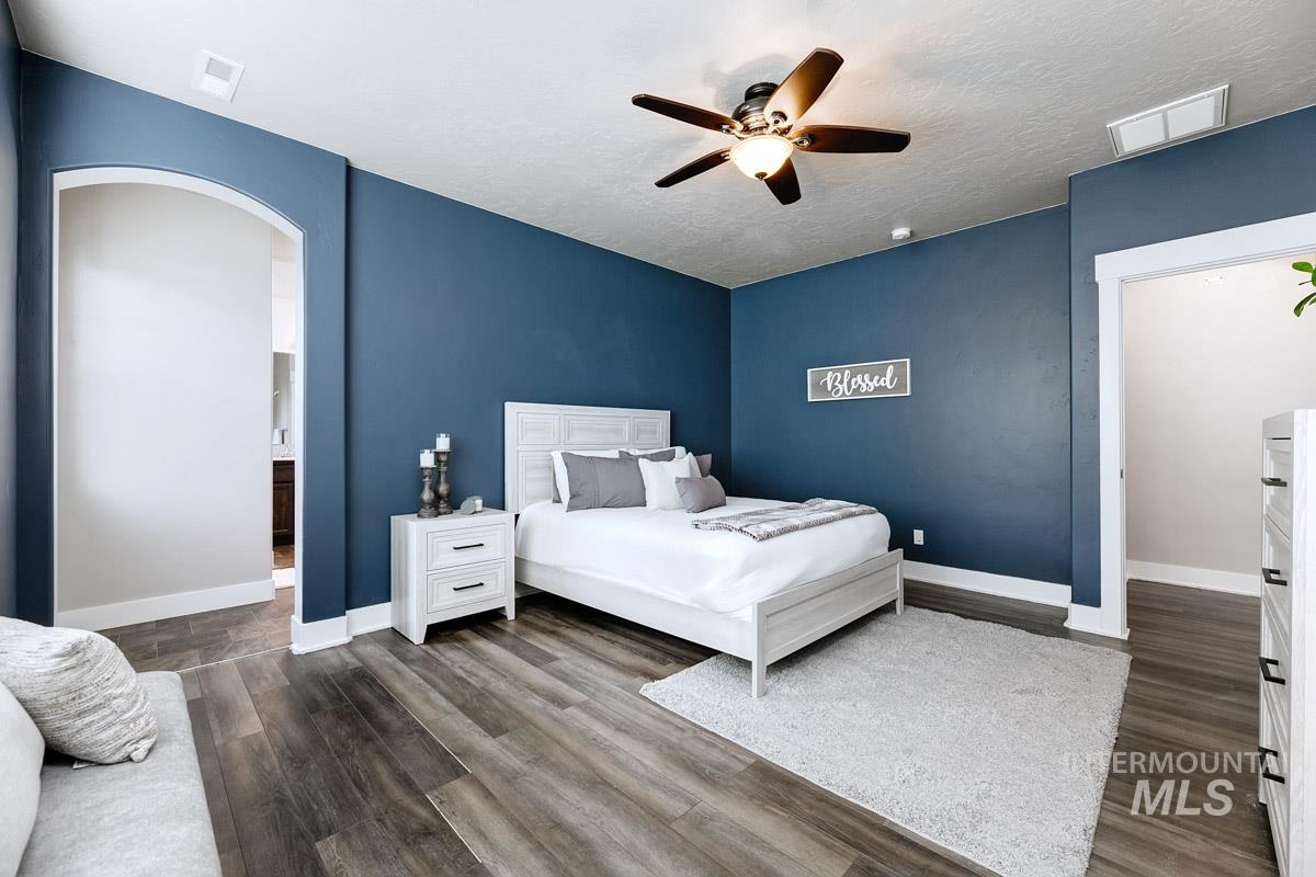 Bedroom with ceiling fan, dark wood finished floors, arched walkways, and a textured ceiling