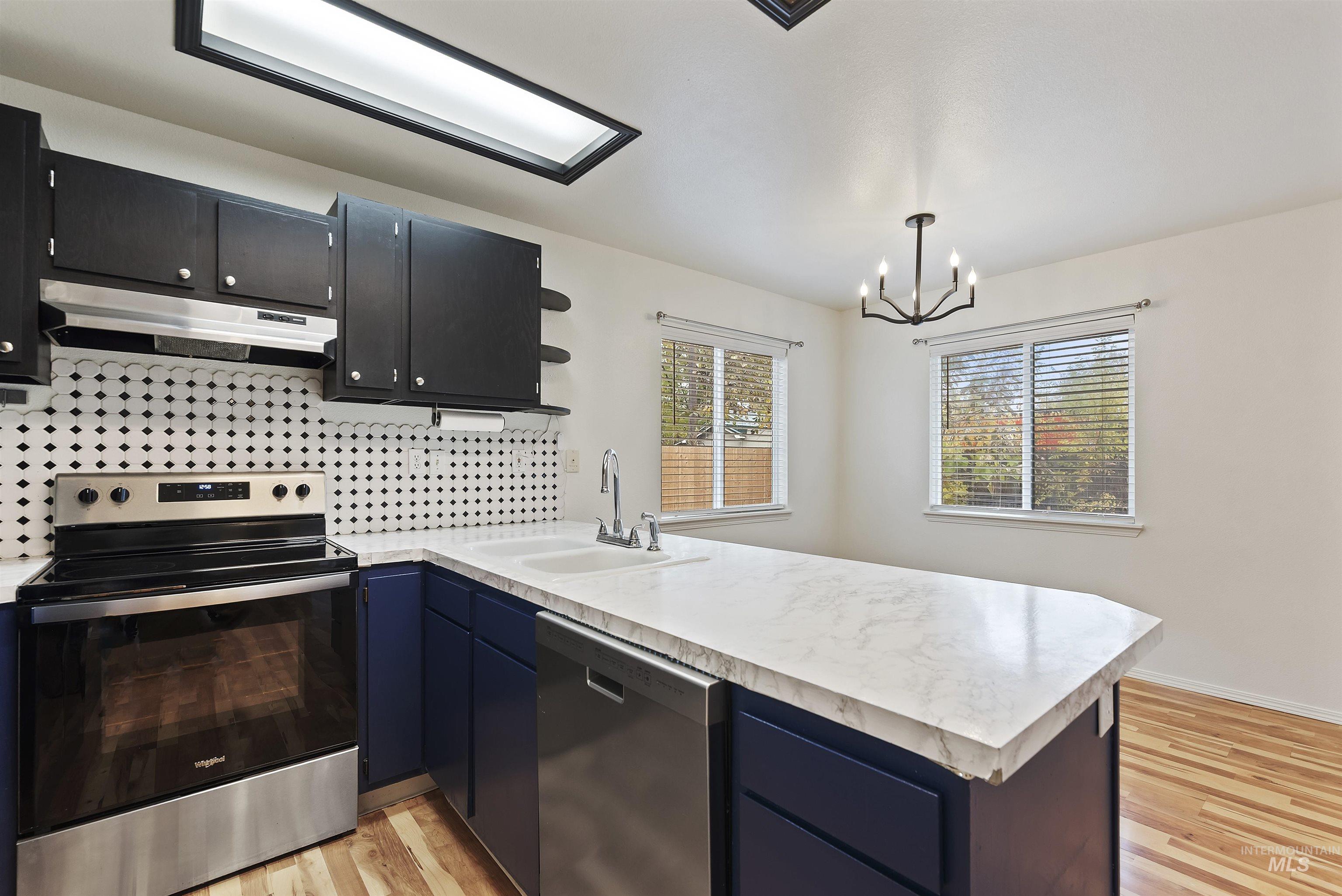 Kitchen featuring appliances with stainless steel finishes, light countertops, tasteful backsplash, under cabinet range hood, and light wood-style floors
