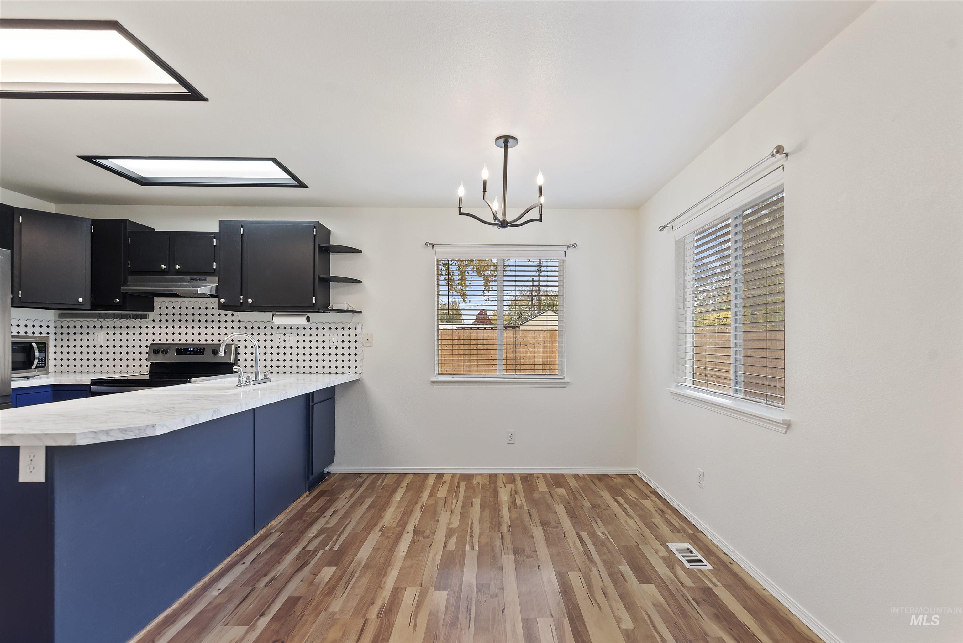 Kitchen with pendant lighting, light countertops, dark cabinetry, a chandelier, and light wood-style flooring