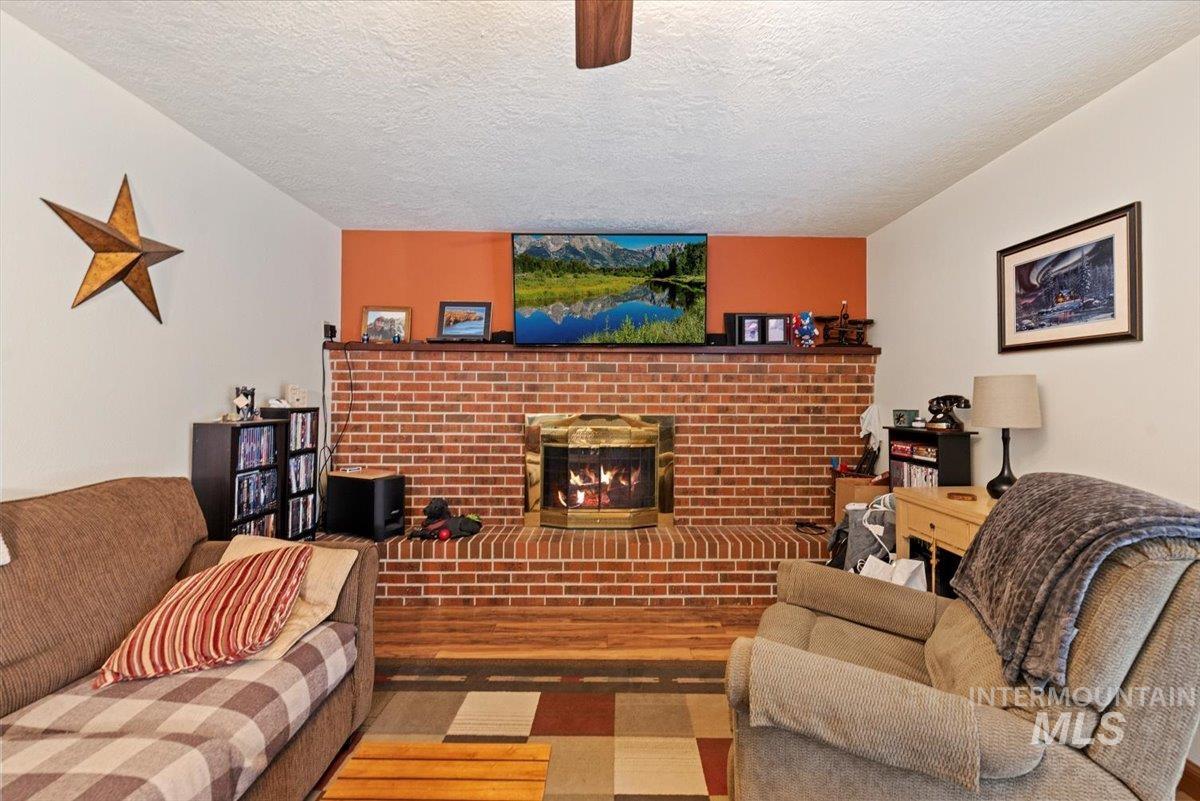 Living room featuring a fireplace, wood finished floors, a textured ceiling, and a ceiling fan
