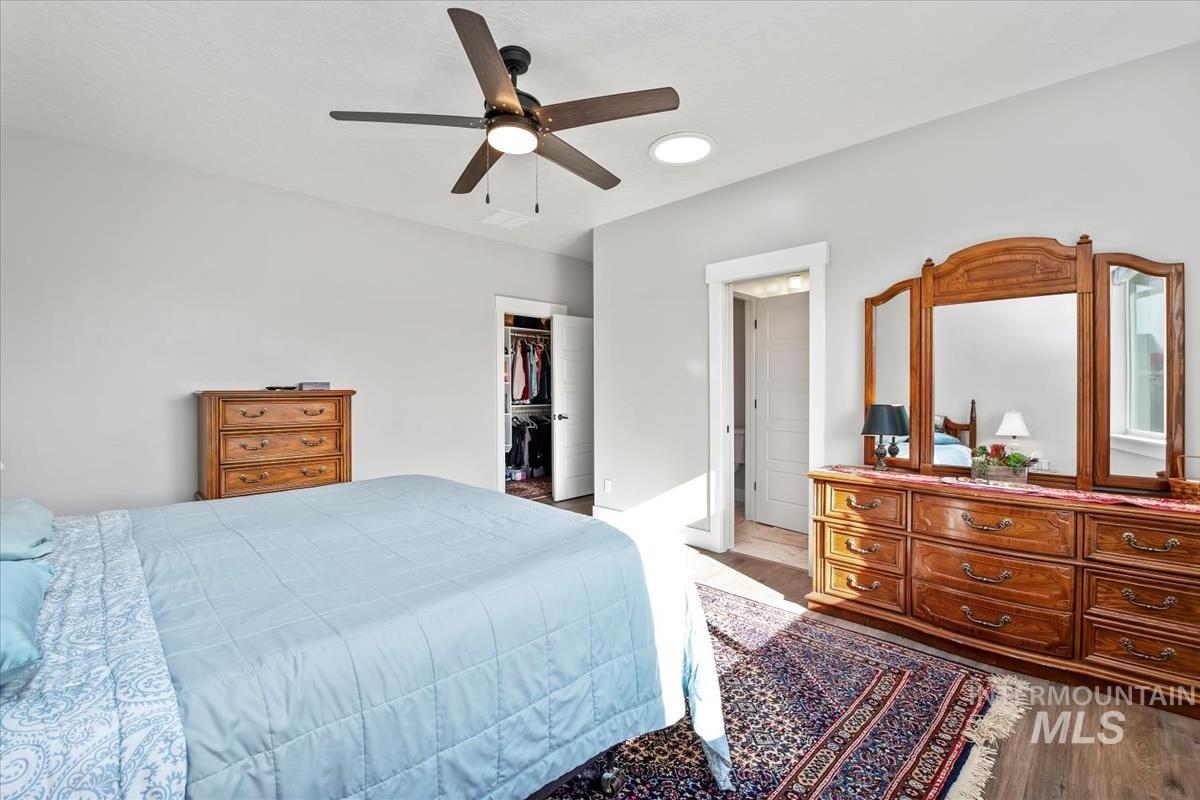 Bedroom with dark wood-style floors, a ceiling fan, and a walk in closet