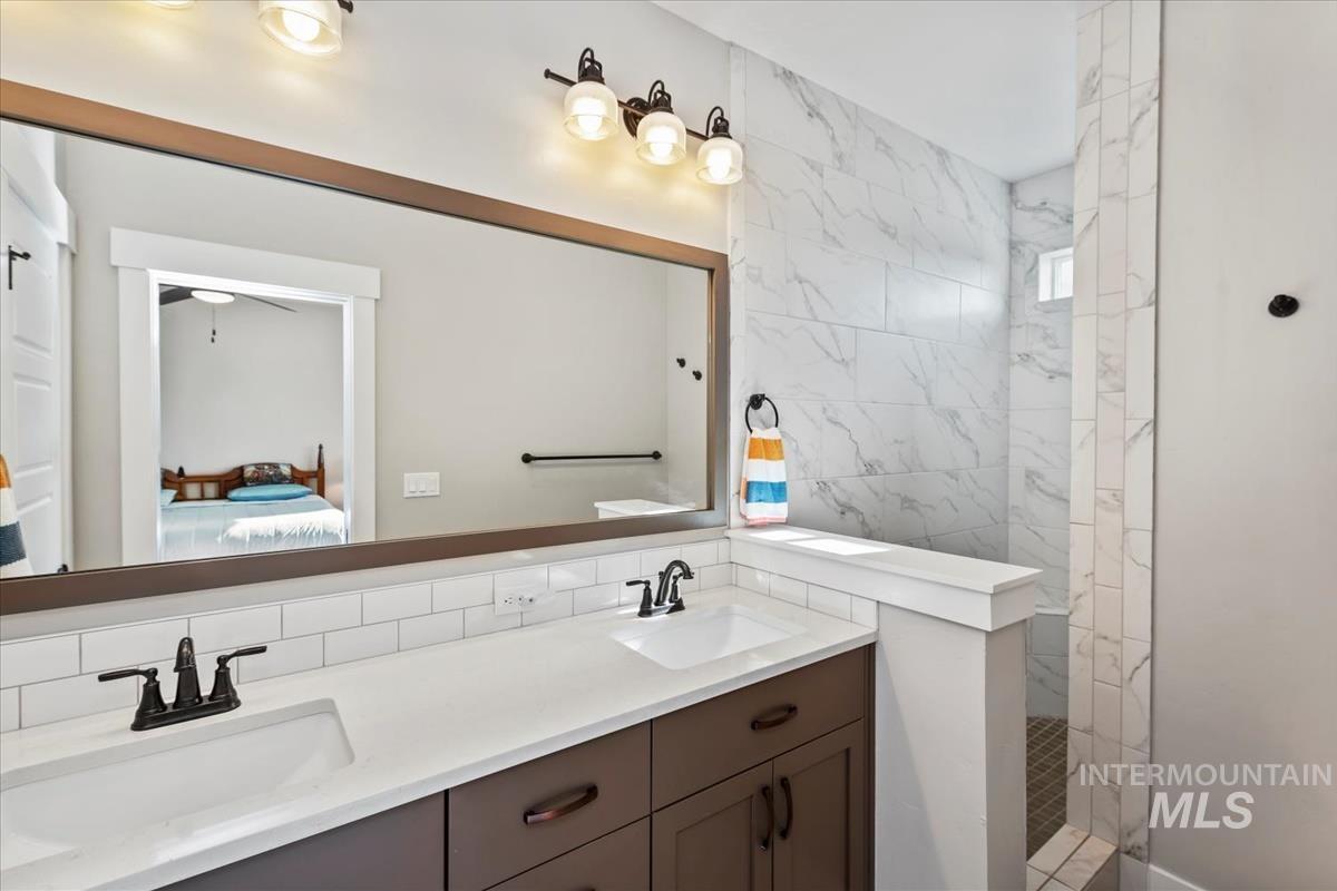 Full bath with double vanity, ensuite bathroom, a marble finish shower, tile walls, and tasteful backsplash