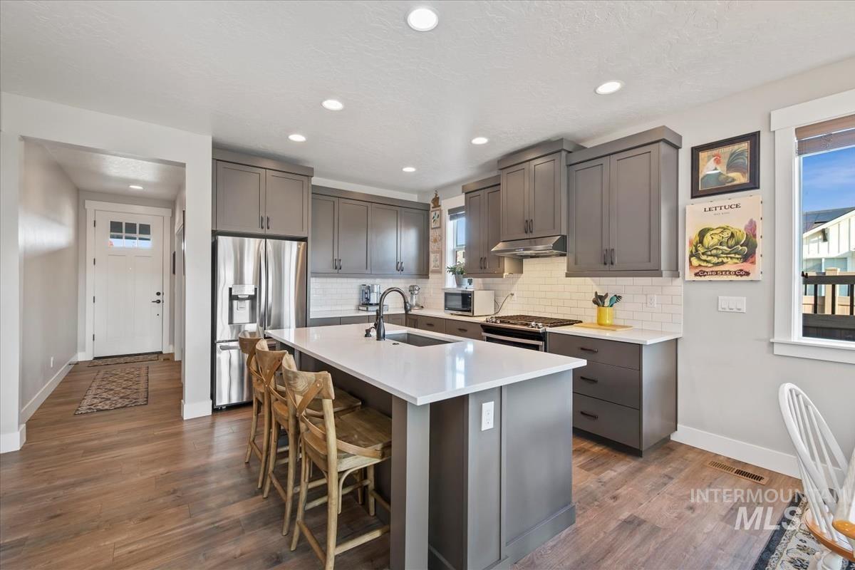 Kitchen featuring stainless steel appliances, gray cabinetry, a kitchen island with sink, decorative backsplash, and recessed lighting