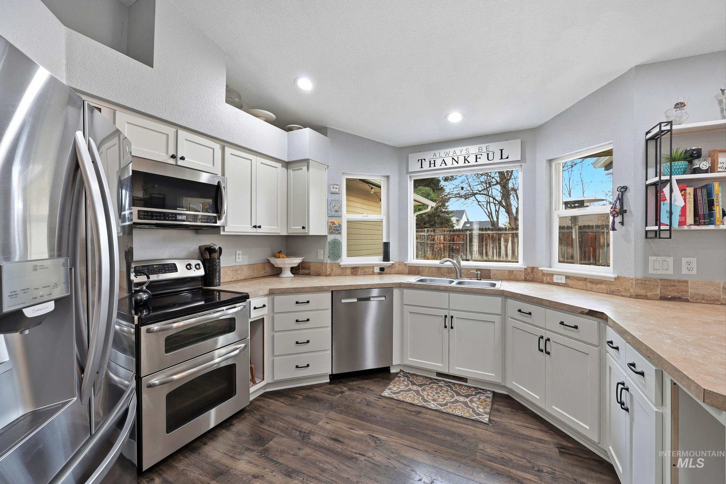 Kitchen featuring appliances with stainless steel finishes, light countertops, white cabinetry, dark wood finished floors, and recessed lighting