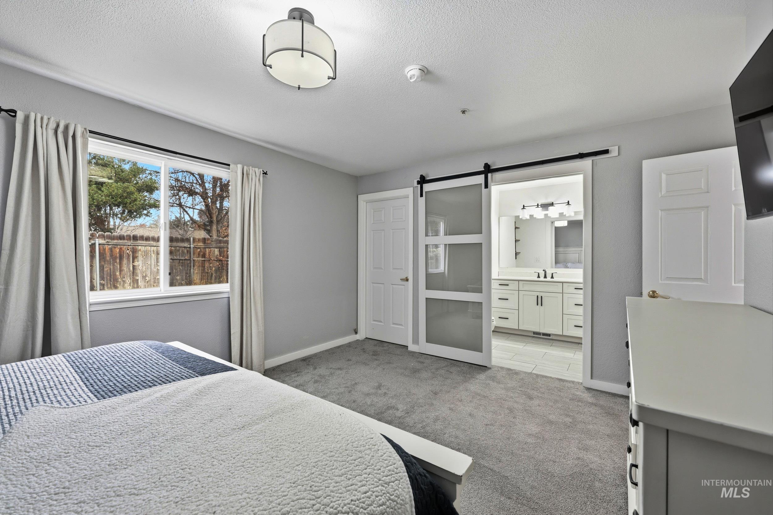 Bedroom with a barn door, light carpet, a textured ceiling, and ensuite bath