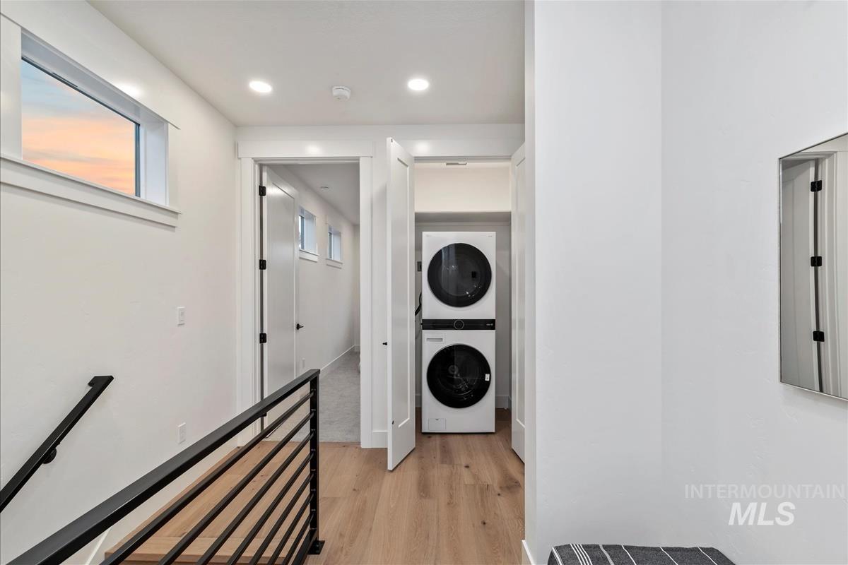Laundry room featuring light wood-type flooring, stacked washer / dryer, and recessed lighting