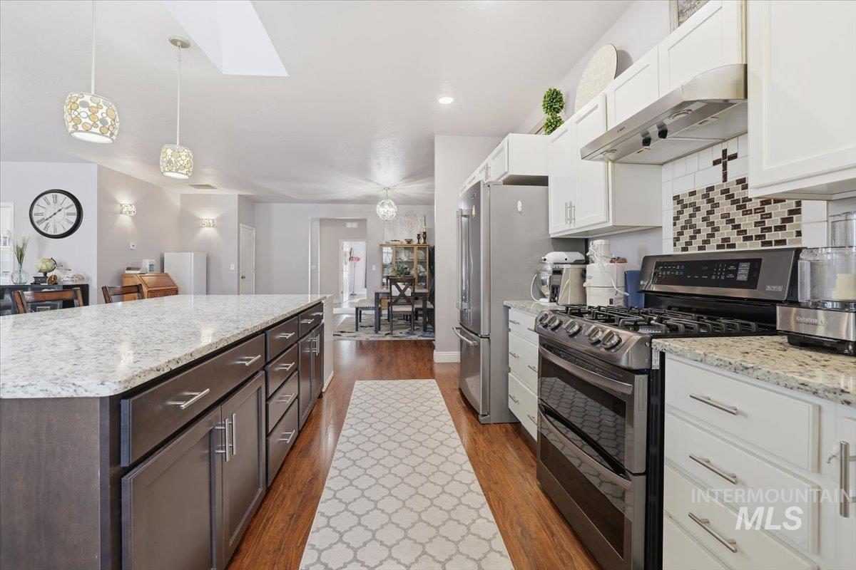 Kitchen with range with two ovens, under cabinet range hood, dark wood finished floors, decorative light fixtures, and recessed lighting