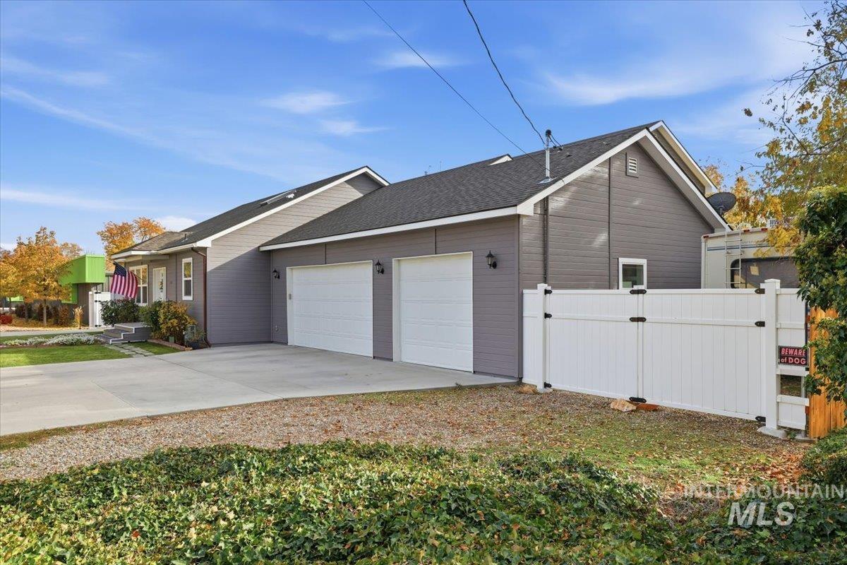 View of side of property with a gate, a garage, driveway, and roof with shingles