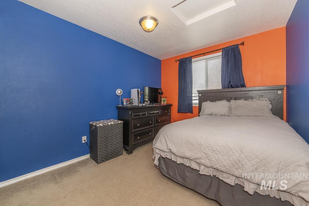 Bedroom with light colored carpet, a textured ceiling, and attic access