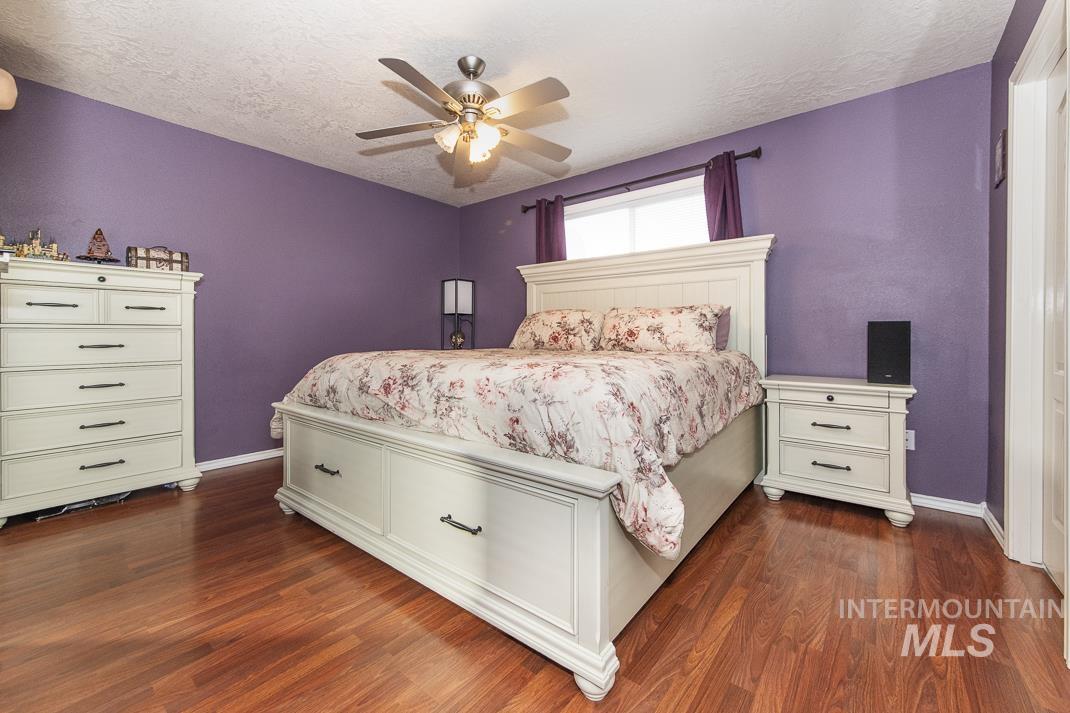 Bedroom with a textured ceiling, dark wood-style flooring, and a ceiling fan
