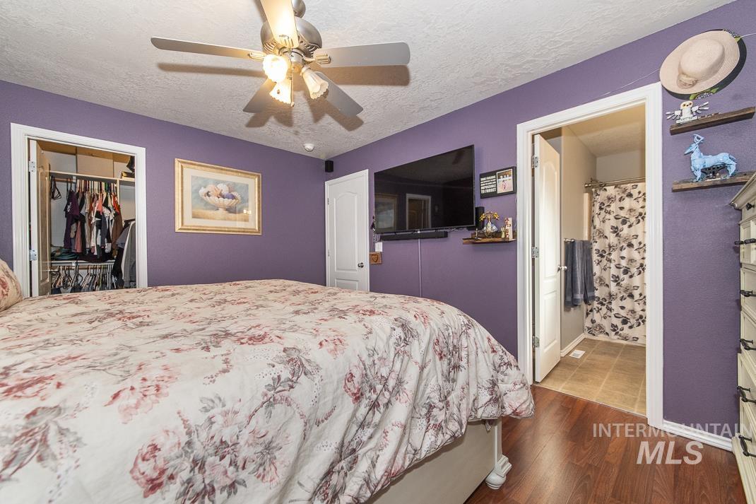 Bedroom featuring dark wood finished floors, a textured ceiling, a ceiling fan, a walk in closet, and ensuite bathroom