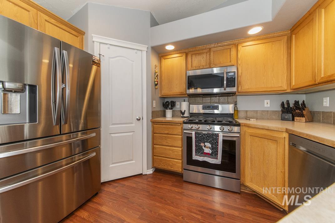 Kitchen with stainless steel appliances, light countertops, dark wood-style flooring, recessed lighting, and brown cabinets