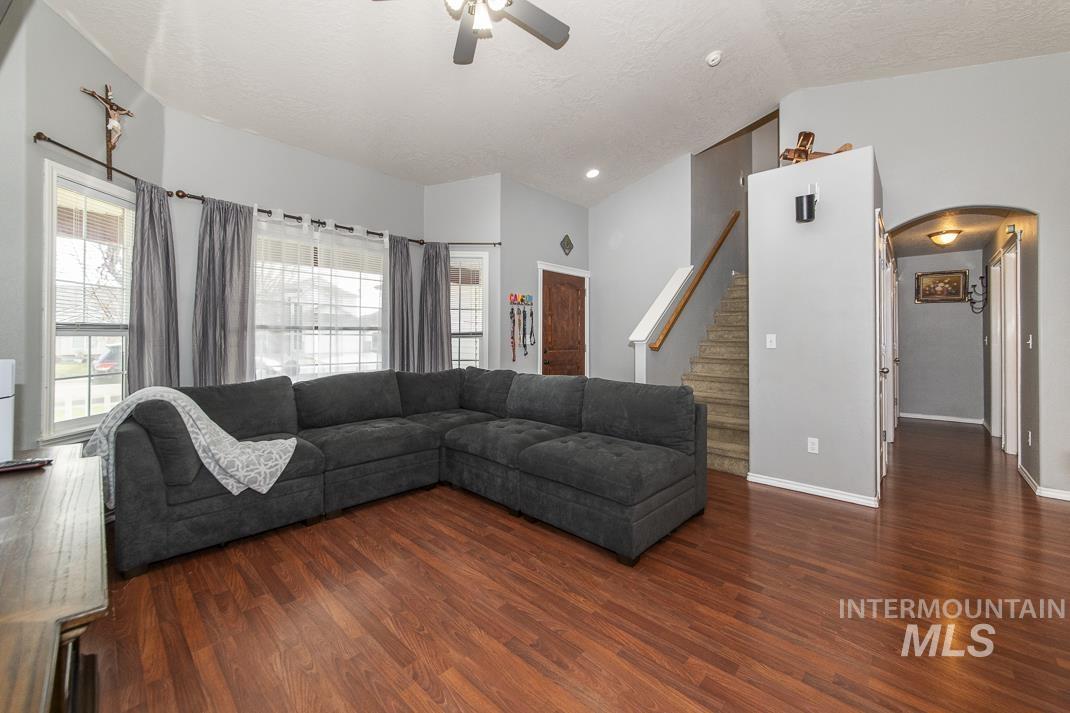 Living room featuring lofted ceiling, stairs, dark wood finished floors, a ceiling fan, and arched walkways