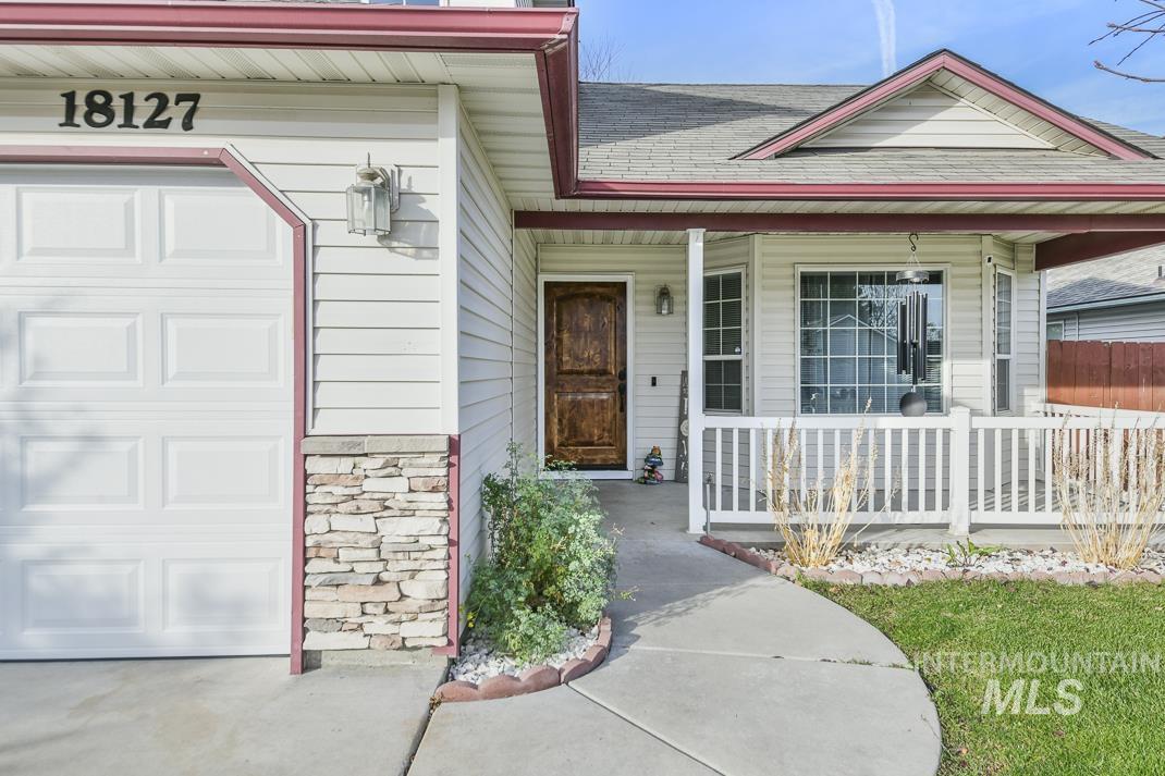 Entrance to property featuring roof with shingles, covered porch, stone siding, and a garage