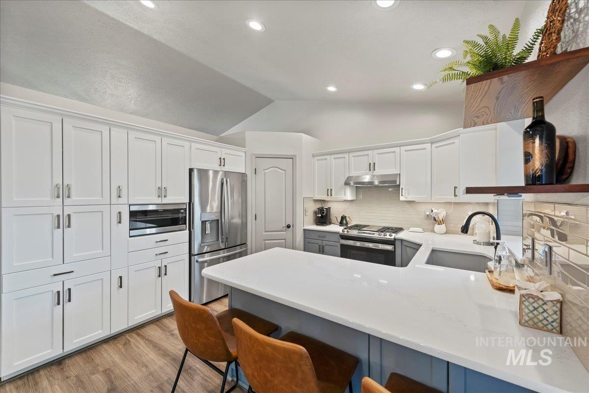 Kitchen featuring stainless steel appliances, vaulted ceiling, decorative backsplash, under cabinet range hood, and a peninsula